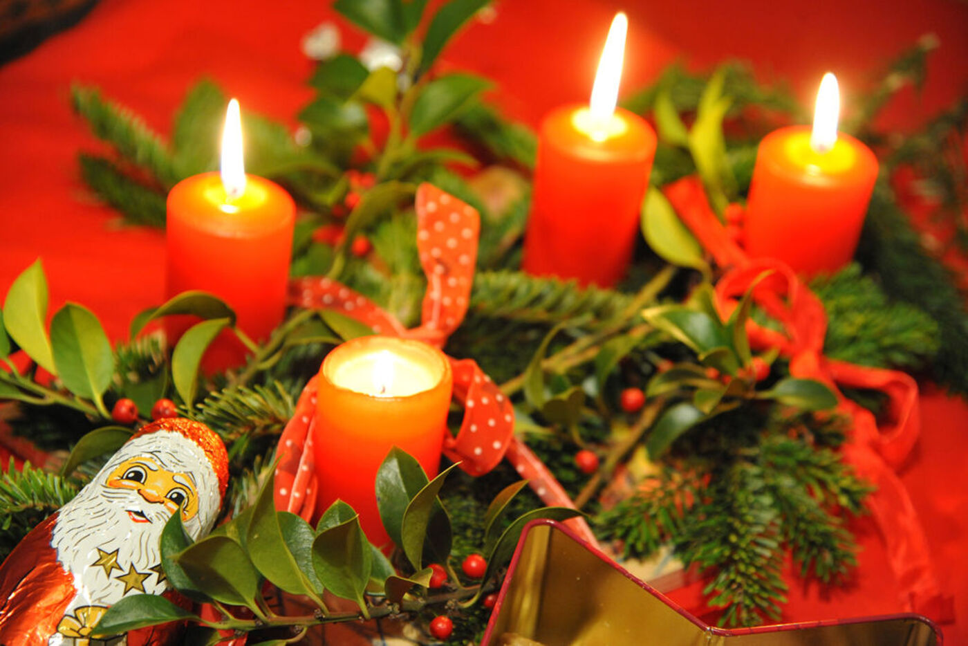 Vier Kerzen auf einem Adventskranz brennen, daneben liegt ein Schoko-Weihnachtsmann.