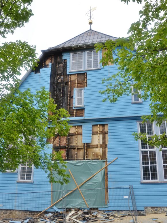Eine blaue Holzkirche, an der Schäden sind.